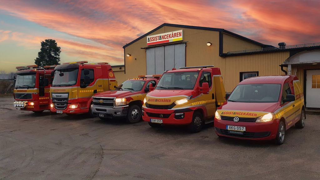 Assistancekårens fordonsflotta framför anläggningen vid solnedgång, professionella bärgningsfordon