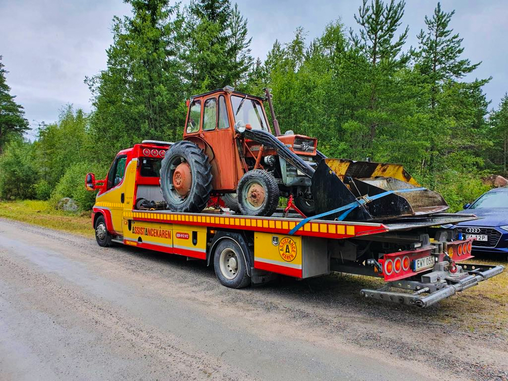 Bärgningsbil som transporterar en traktor på skogsväg, specialtransport i Söderhamn